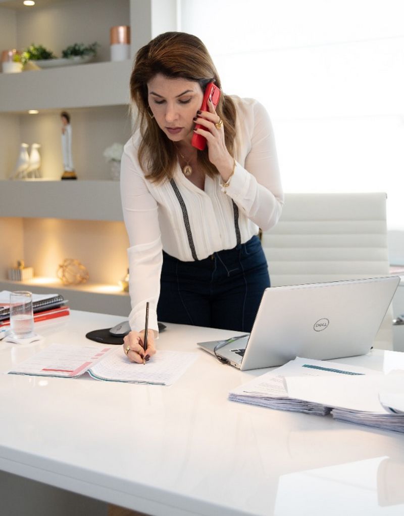 Foto de Manoela Peres em seu gabinete, falando ao telefone e fazendo uma anotação.